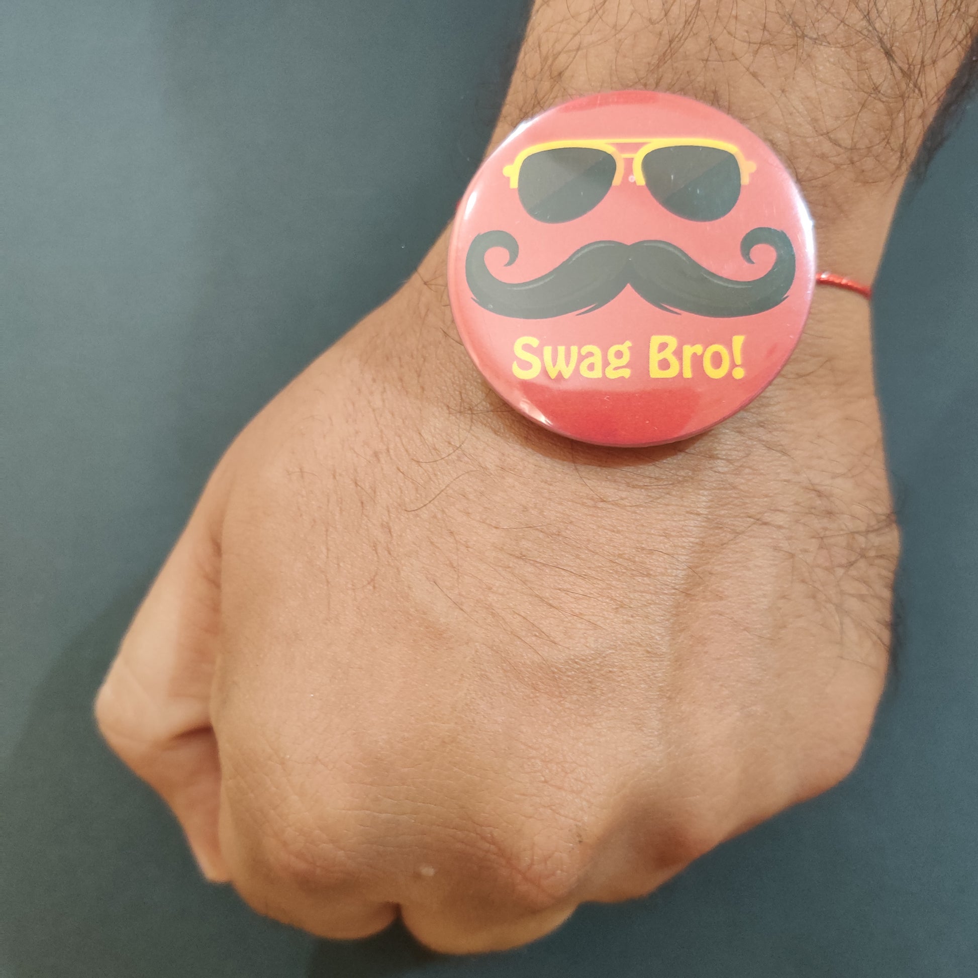 Close-up detail of 'Swag Bro' inscription on metal Rakhi and magnet.