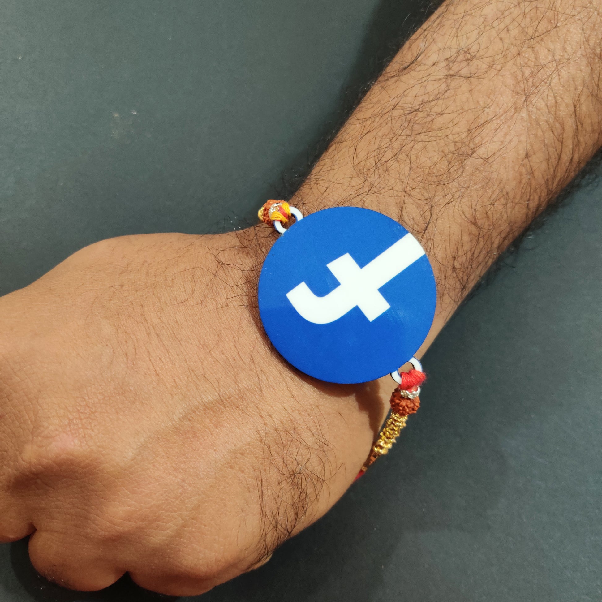 Trendy Facebook Wooden Rakhi with Rudraksha thread worn on a brother's wrist, perhaps near a smartphone.
