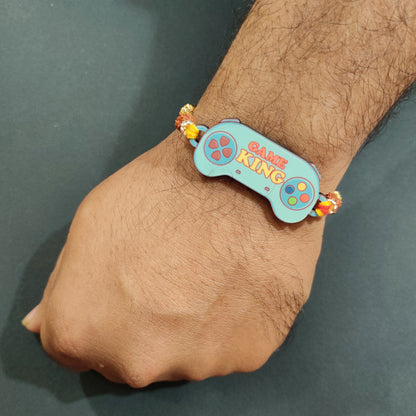 Cool Gamer King Bhai Wooden Rakhi with Rudraksha thread worn on a brother's wrist, perhaps near a gaming controller.