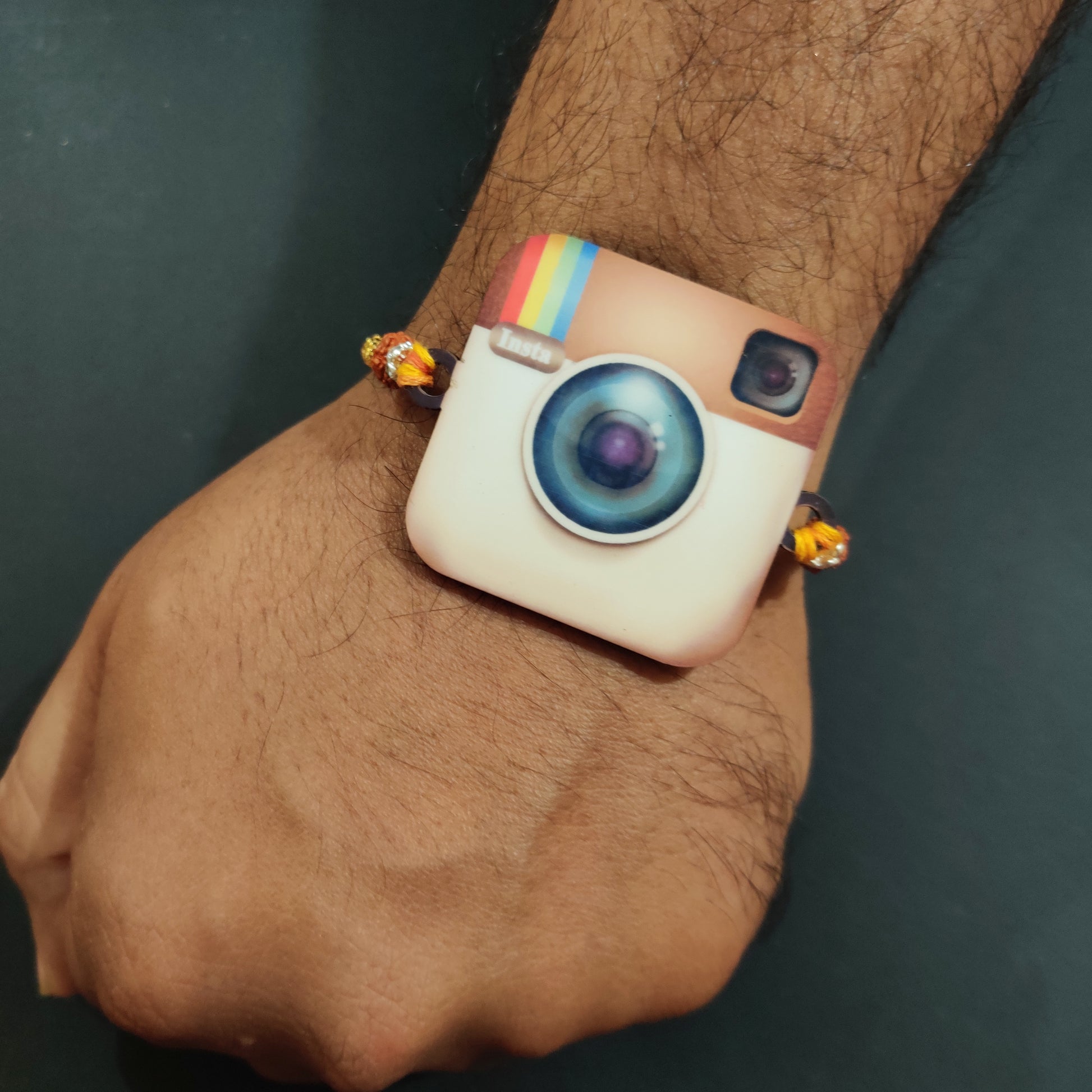 Trendy Insta Wala Bhai Wooden Rakhi with Rudraksha thread worn on a brother's wrist, perhaps near a phone