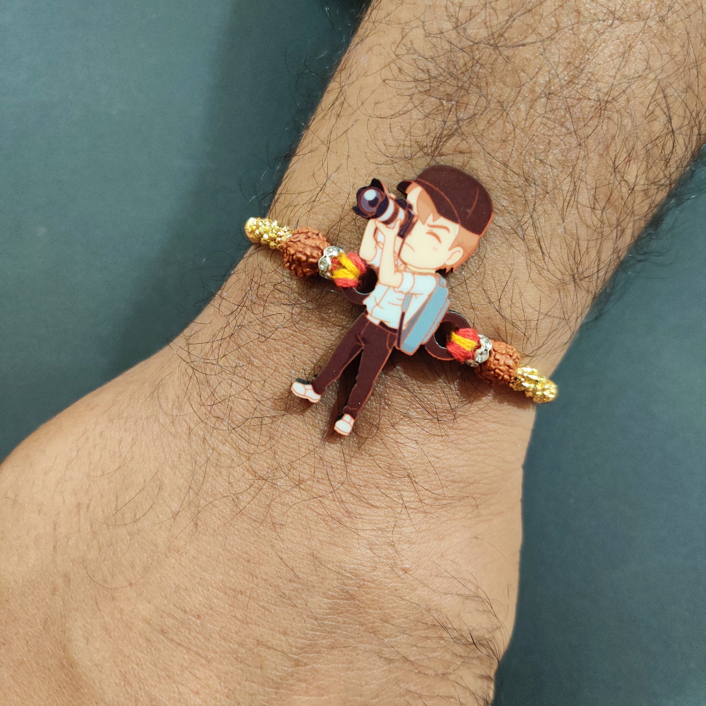 Photographer Bhai Wooden Rakhi with Rudraksha thread worn on a brother's wrist, perhaps holding a camera.